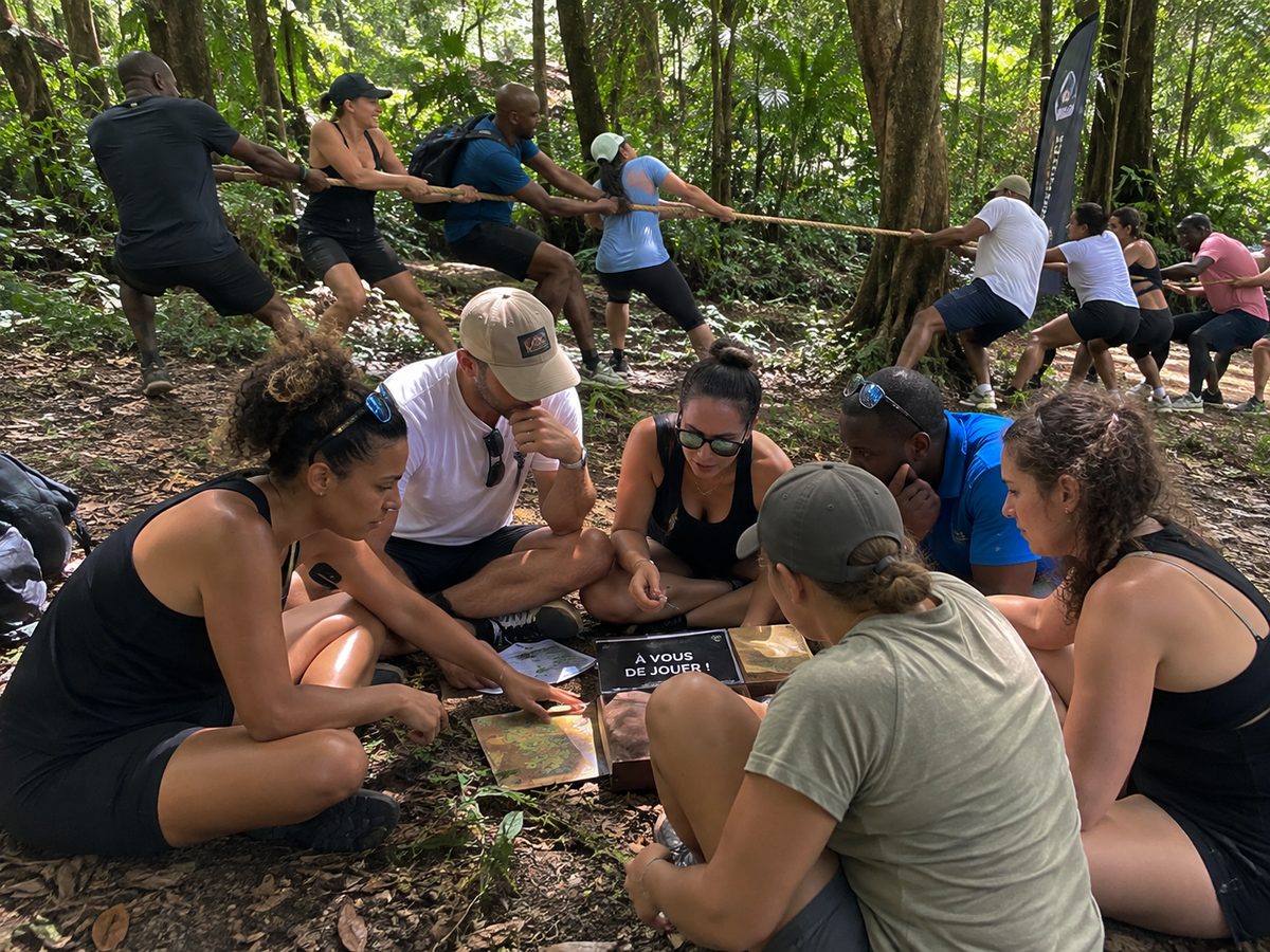 Équipe en plein air lors d’un team building : un groupe assis autour d’un jeu collectif, un autre tirant à la corde en forêt